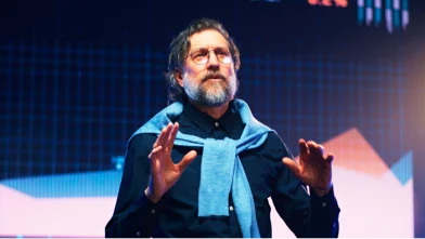 A bearded man speaks on stage with his hands raised